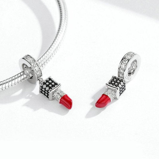 Pair of lipstick charms with red enamel and sparkling stones shown on a silver bracelet, perfect accessory for beauty enthusiasts.