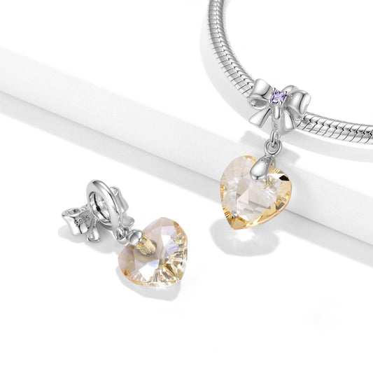 Elegant Golden Crystal Charm displayed on a silver bracelet, featuring a heart-shaped gemstone and bow detail. Ideal for jewelry lovers.