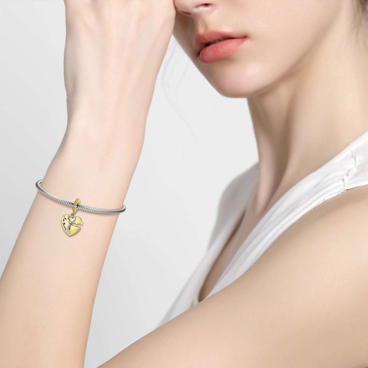 Model wearing Love Lock Charm on a silver bracelet. Heart-shaped gold charm adds a romantic touch to any jewelry collection.