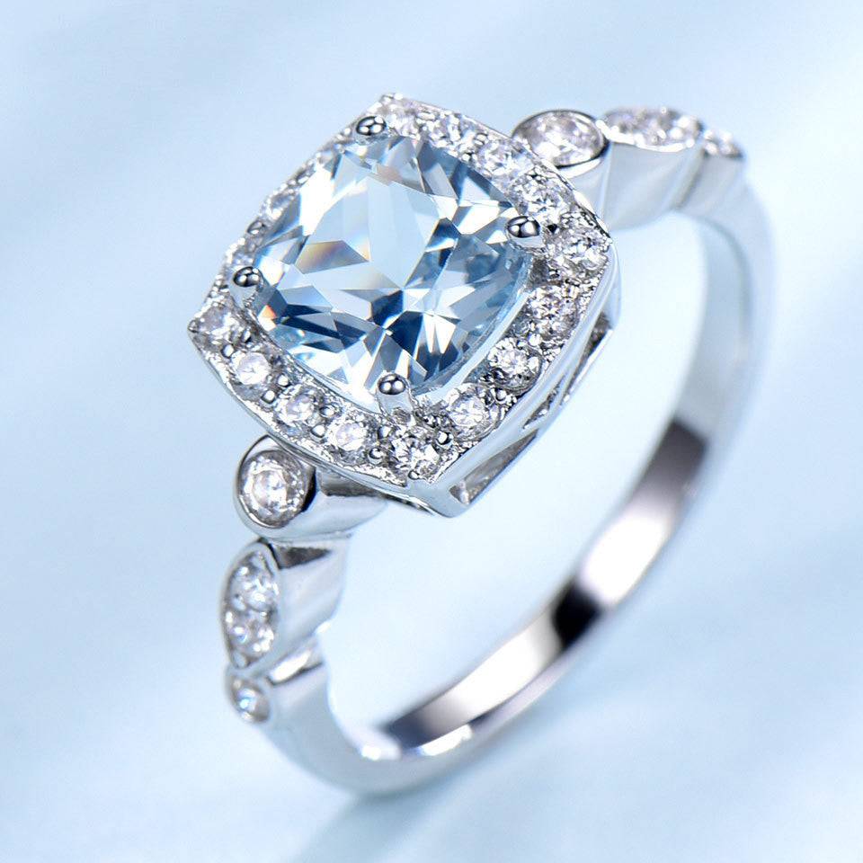 Angled view of Sterling Silver Blue Topaz Ring with shimmering halo and detailed band, perfect for elegant and durable wear.