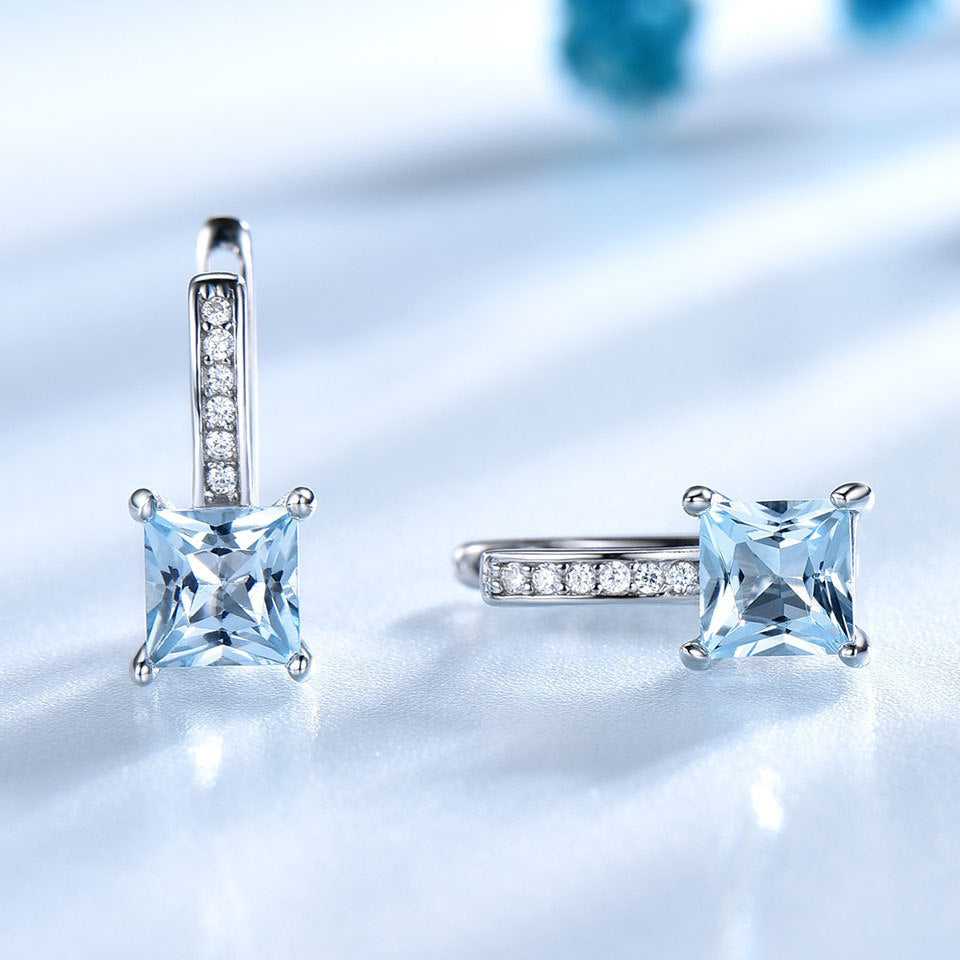 Sky Blue Topaz Earrings - Silver Craftsmanship displayed on a reflective surface, showcasing the brilliance of the gemstones and polished silver finish.