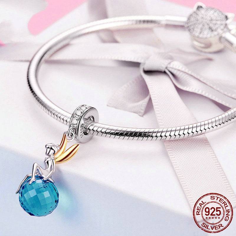 Blue Crystal Fairy Charm attached to a sterling silver bracelet, showcasing a faceted blue gemstone and a delicate fairy design with gold-tone wings.