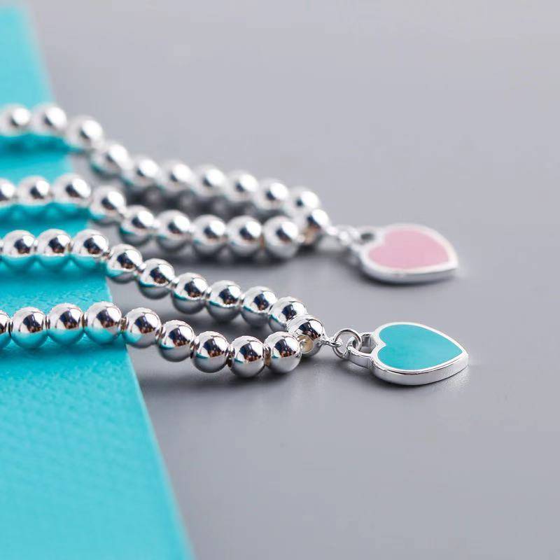 Close-up of silver heart tag bracelets with turquoise and pink enamel charms, elegant jewellery for personalised gifting.