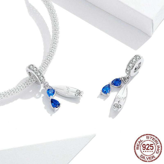 Fun Surfboard Charm in sterling silver with blue sunglasses detail, shown with and without bracelet. Ideal for beach-themed jewelry collections.