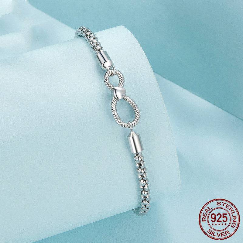 Close-up of Infinity Knot Silver Bracelet draped on a rolled fabric, showcasing intricate braided design and infinity clasp in 925 sterling silver.