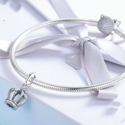 Dangle Crown Charm on silver bracelet with ribbon accent, perfect for adding a royal touch to your jewelry collection. Ideal for charm bracelets or necklaces.