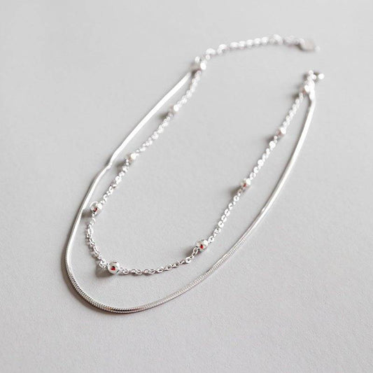 Flat lay of Elegant Double Round Bead Anklet in sterling silver, showcasing its sleek dual-chain design with polished round beads.