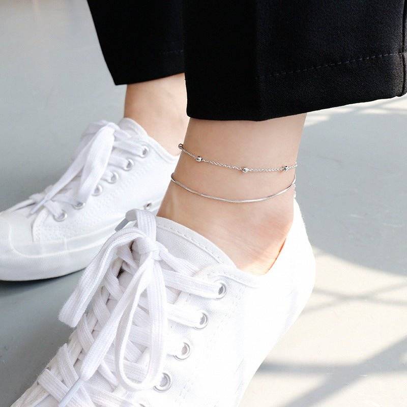 Minimalist Double Round Bead Anklet styled on ankle with white sneakers, showcasing its elegant silver charm for casual or chic outfits.