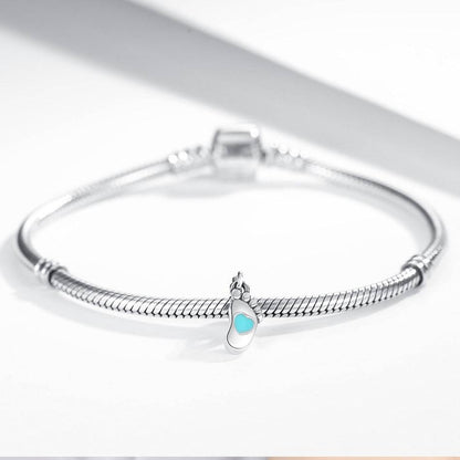 Baby footprint charm attached to a sterling silver bracelet, featuring a turquoise heart detail. A meaningful jewelry piece for parents.