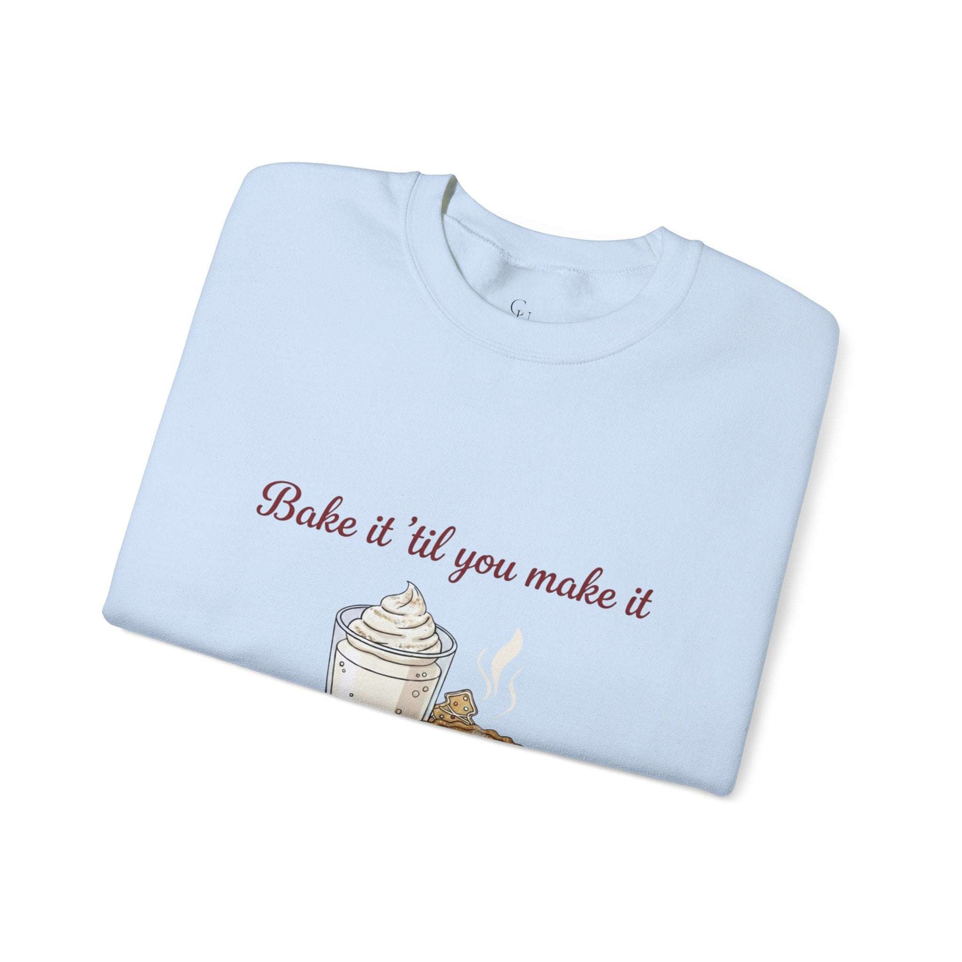 Women’s sweatshirt folded neatly with 'Bake it ‘til you make it' embroidered above a whipped dessert and cookie graphic. Cozy and festive for wine lovers.