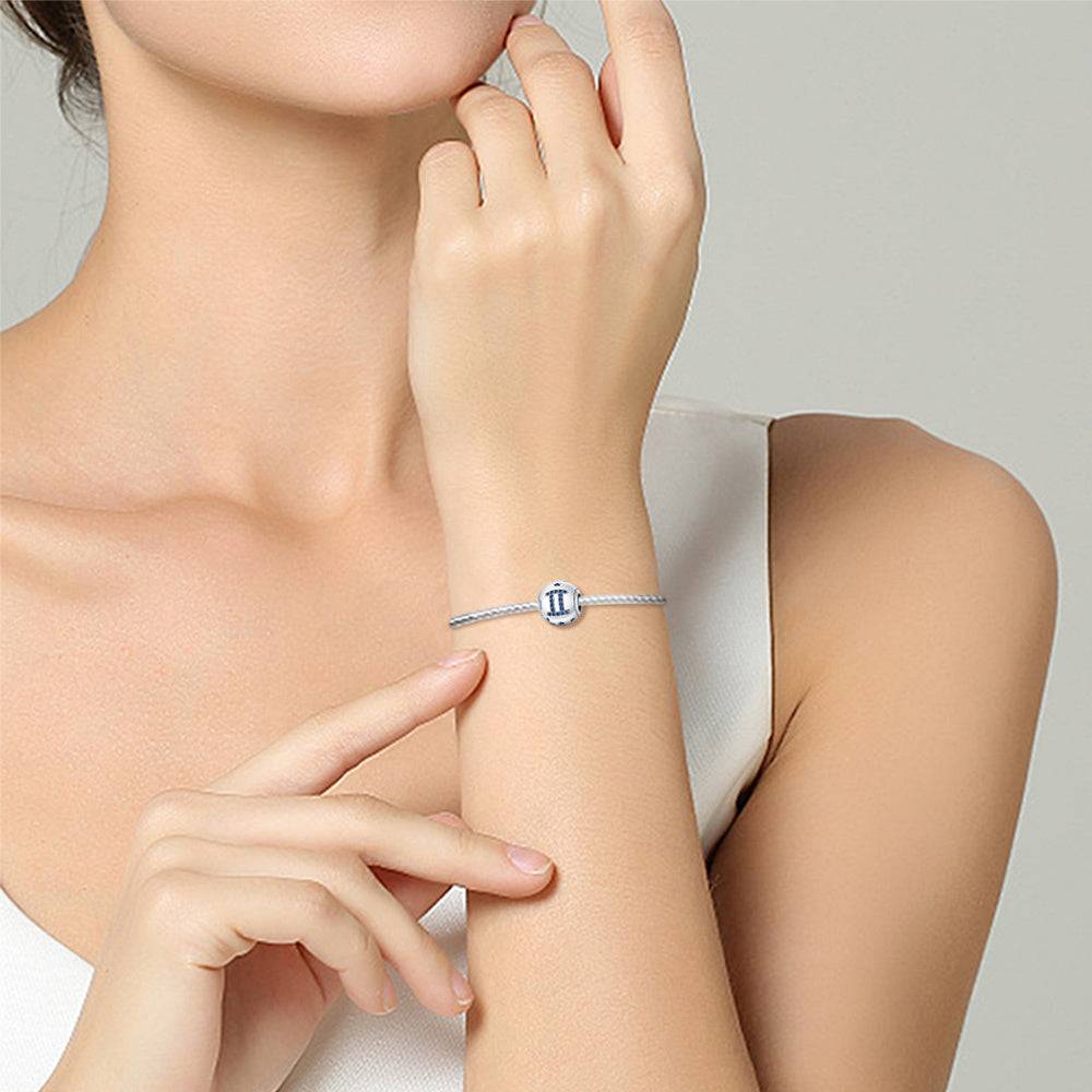 Woman wearing a Gemini zodiac charm bracelet in sterling silver, showcasing a sleek and stylish personalized jewelry accessory.