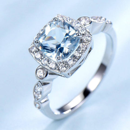 Angled view of Sterling Silver Blue Topaz Ring with shimmering halo and detailed band, perfect for elegant and durable wear.