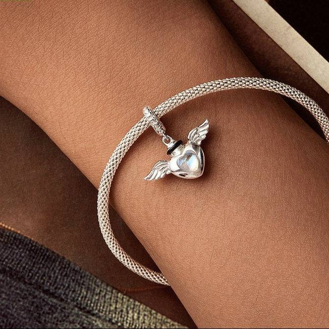 Silver bracelet with a heart-shaped pendant on a wrist against a neutral background